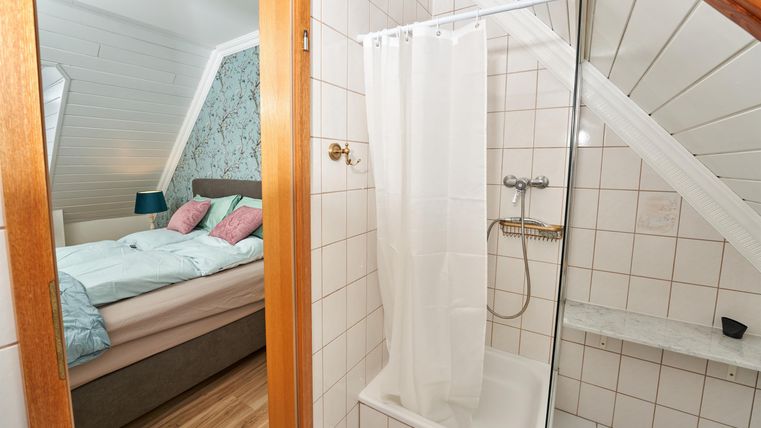 A modern bathroom with a shower and adjoining bedroom. The walls are brightly tiled and there is a cozy atmosphere.
