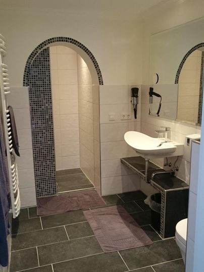 Ein modernes Badezimmer mit einer geräumigen Dusche und einem Doppelwaschbecken. Der Boden ist mit dunklen Fliesen ausgelegt und es gibt helle Wände.