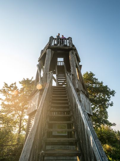 Holzaussichtsturm mit Personen oben, blauer Himmel.