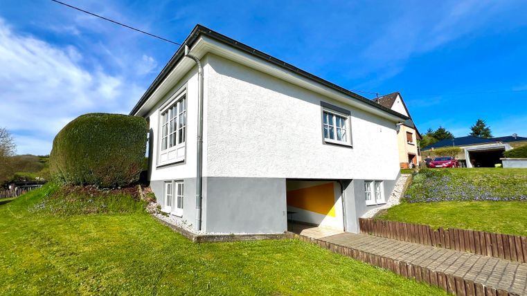 A modern, white house with a green lawn and clear sky. The surroundings are quiet and well-maintained.