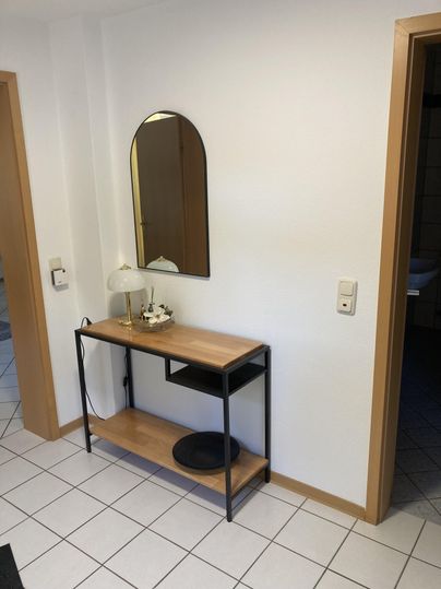 A modern hallway with a stylish table and a round mirror. The walls are white, and the floor is covered with tiles.