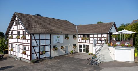 A modern half-timbered house with a terrace and flower windows. There is a clear blue sky and a small bike rack.