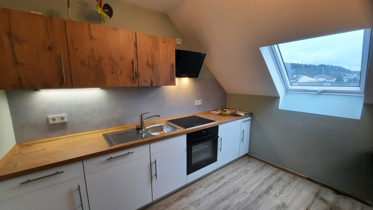 A modern kitchen with wooden and white furniture. The window offers a view of the landscape.