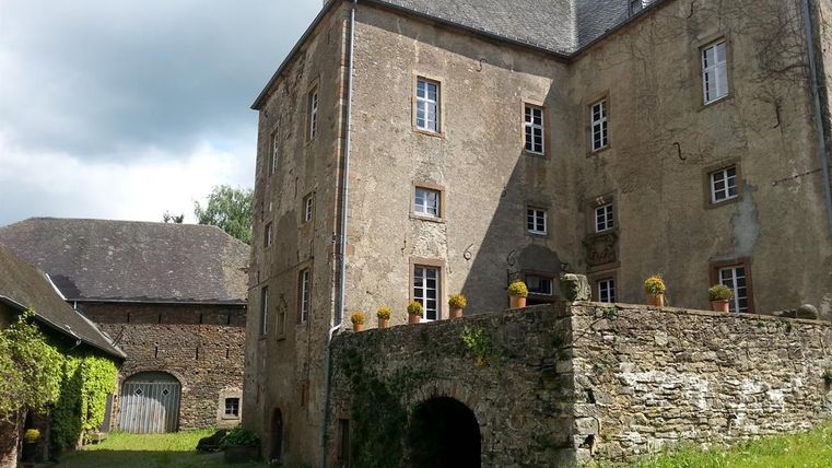 Historische Burg Lissingen mit massiven Steinmauern, Fenstern und einem begrünten Innenhof unter bewölktem Himmel.