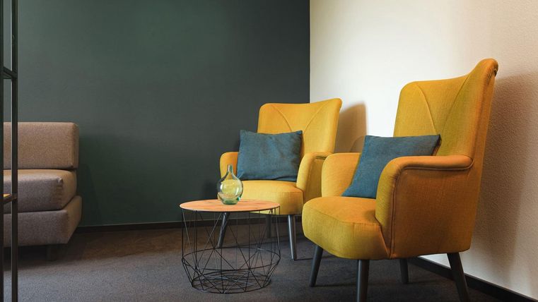 Een stijlvolle ruimte met twee gele stoelen en een kleine tafel. De muren hebben een donkere kleur die een gezellige sfeer creëert.