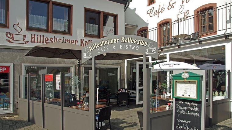 Ein charmantes Café mit einem einladenden Außenbereich. Die Fassade zeigt den Namen "Hillesheimer Kaffeestüble" und lädt zum Verweilen ein.