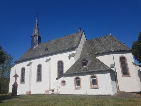A historic church with a steep roof and a small outbuilding. The sky is clear and blue, surrounded by green grass.