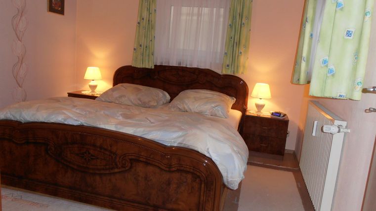 Ein gemütliches Schlafzimmer mit einem großen Holzbett und zwei Nachttischlampen. Die Wände sind in sanften Farben gehalten, und die Vorhänge sind blumig dekoriert.