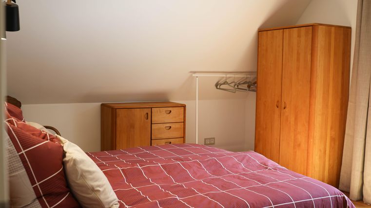 A cozy attic bedroom with a double bed and wood-colored furniture. The room is bright and airy with a soft light.