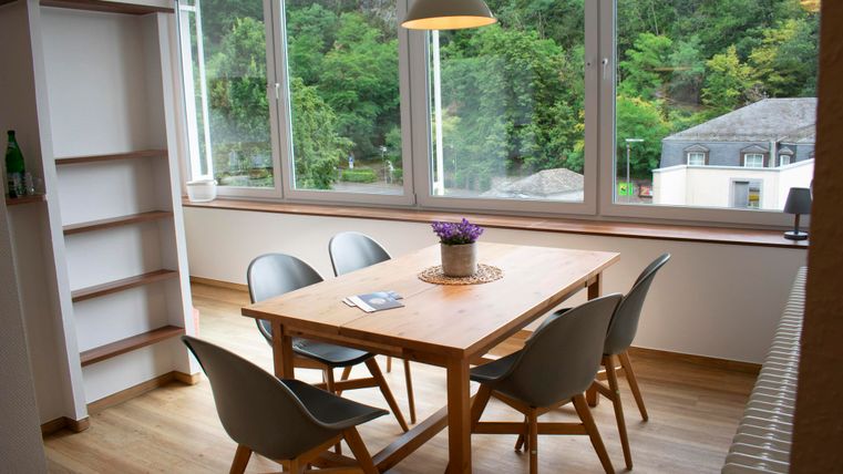 Ein moderner Essbereich mit einem Holztisch und Stühlen. Große Fenster bieten einen Blick auf die grüne Landschaft draußen.