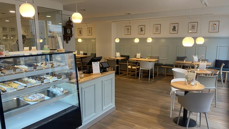 Een modern café met een vitrine vol lekkernijen. De inrichting is helder en vriendelijk, met gezellige zitplaatsen.