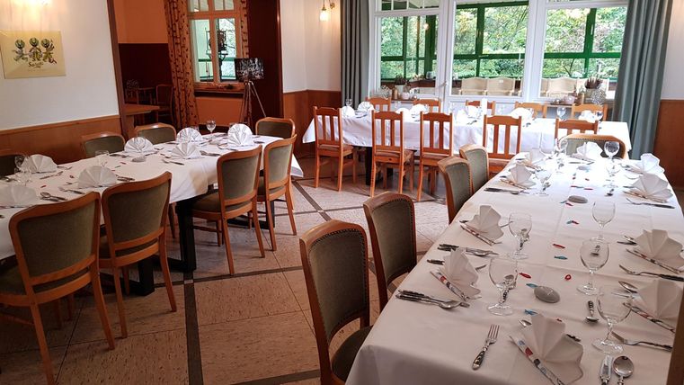 Een elegante eetzaal met meerdere gedekte tafels. De sfeer is vriendelijk en uitnodigend, met veel natuurlijk licht.