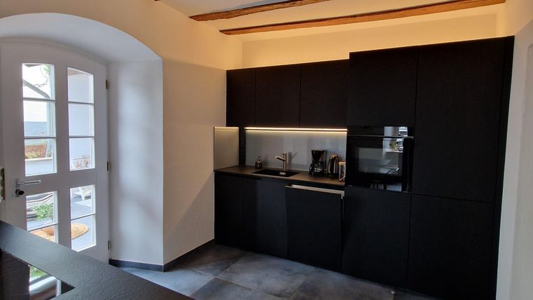A modern kitchen with black furniture and a wooden ceiling. It is bright and spacious, with an open window front.