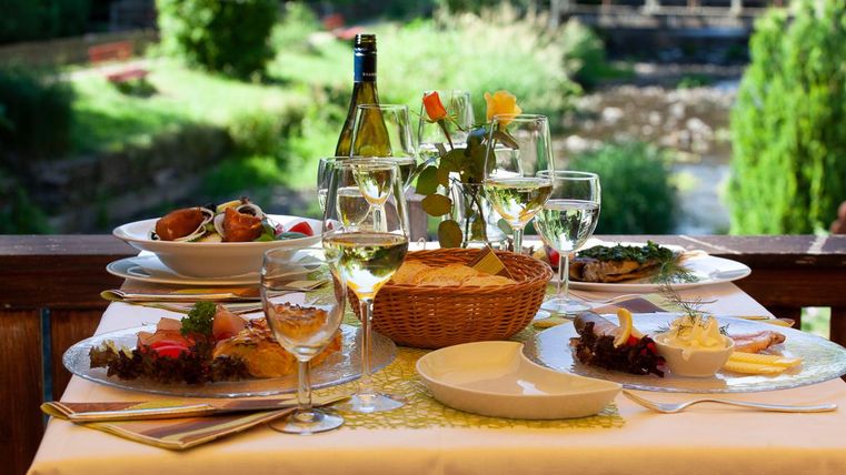 Ein elegant gedeckter Tisch mit köstlichem Essen und Weingläsern. Im Hintergrund ist eine grüne Landschaft zu sehen.