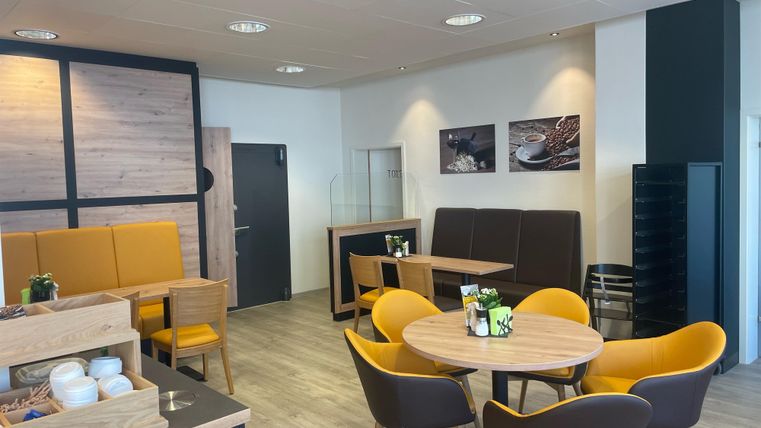 Een modern café met heldere kleuren en gezellige zitgedeelten. De inrichting omvat houten meubels en planten op de tafels.