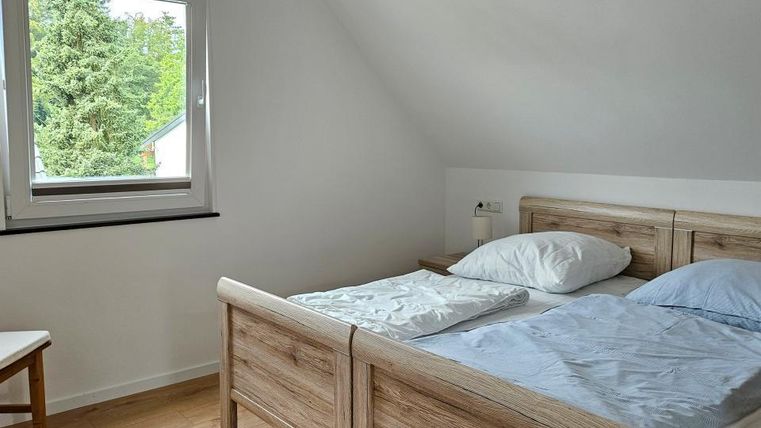 Ein heller Schlafzimmer mit einem Doppelbett und einer großen Fensterfront. Der Raum hat eine moderne, schlichte Einrichtung und einen Blick ins Freie.