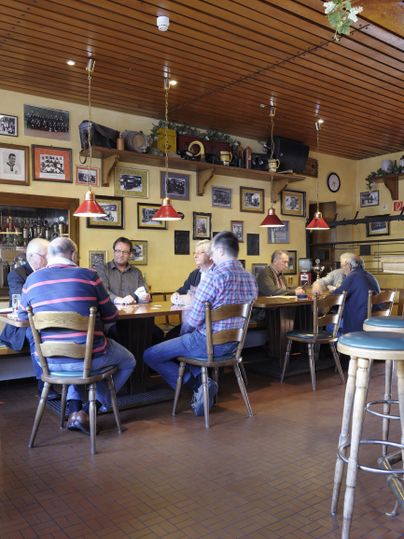 Eine gemütliche Bar mit mehreren Männern, die an der Theke sitzen. Die Wände sind mit verschiedenen Bildern und Dekorationen geschmückt.