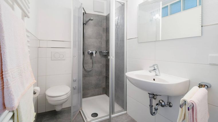 A modern bathroom with a shower, a sink, and a toilet. The walls are light, and there are towels in soft colors.