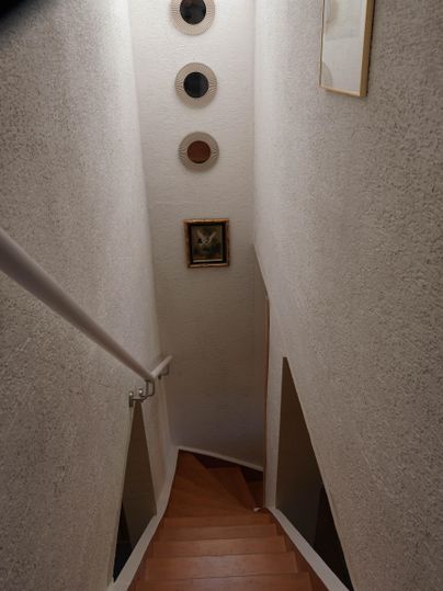 Eine helle Treppe mit Holzstufen führt nach unten. An der Wand hängen runde Bilder und ein kleines gerahmtes Bild ist sichtbar.