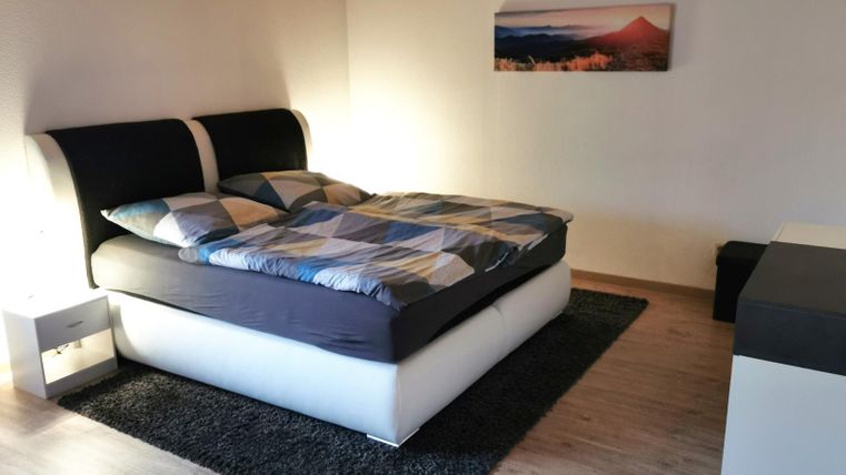 A modern bedroom with a double bed and colorful bedding. The room has a cozy carpet and a calm atmosphere.