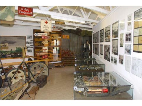 Ein Museum mit historischen Artefakten, darunter Werkzeuge und Fotografien an den Wänden. In der Mitte steht eine Statue, umgeben von Vitrinen mit verschiedenen Ausstellungsstücken.