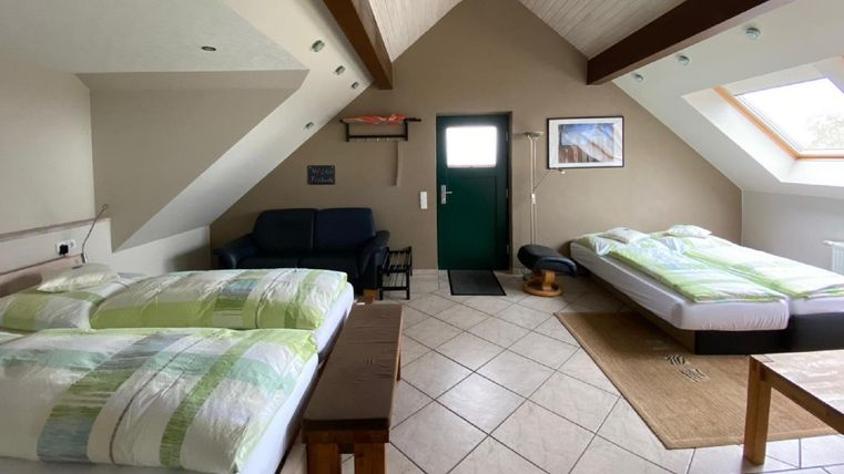 Ein gemütliches Zimmer mit zwei Einzelbetten und einem Schlafsofa. Große Fenster sorgen für viel Tageslicht und eine angenehme Atmosphäre.