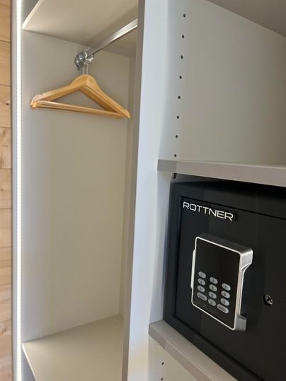 Ein offenes Schrankfach mit einem Kleiderbügel und einem integrierten Safe. Der Safe ist elektronisch gesichert und bietet Platz für Wertgegenstände.