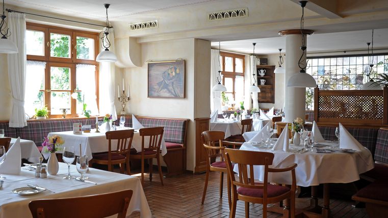Ein gemütliches Restaurant mit Holzstühlen und Tischen, die elegant gedeckt sind. Große Fenster lassen viel Tageslicht herein und bieten eine einladende Atmosphäre.
