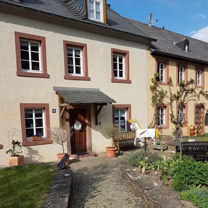 Ein charmantes Haus mit einem begrünte Vorgarten. Die Fassade ist hell und mit braunen Fensterrahmen gestaltet.