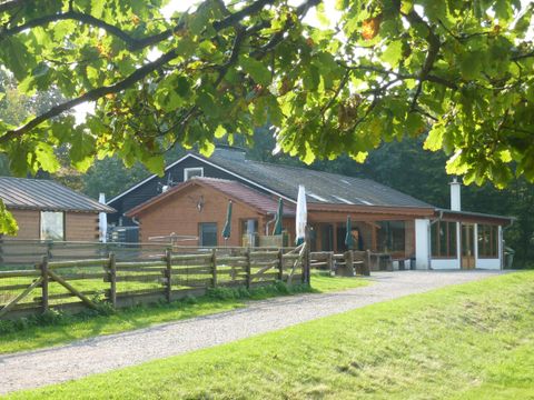 Een rustiek gebouw op een uitgestrekt terrein. Omgeven door bomen en een hek, straalt het een uitnodigende sfeer uit.