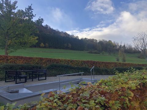 Een rustige landschap met uitzicht op groene weilanden en bomen. Op de voorgrond staan moderne zitgelegenheden op een geplaveid gebied.