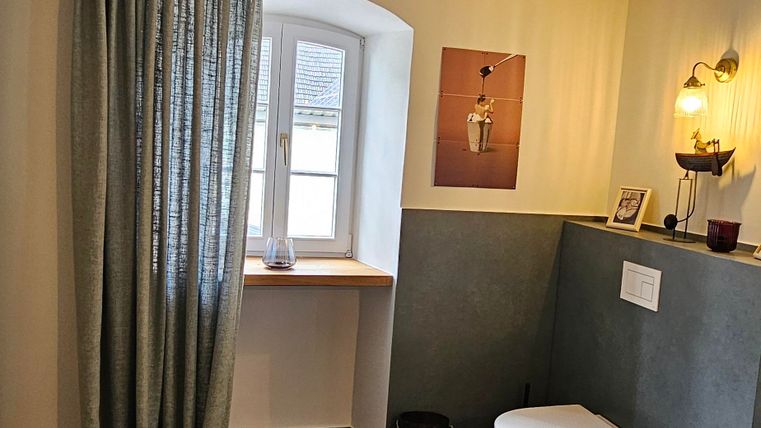 A modern bathroom with a large window and a beautiful view. It is bright and friendly designed, with a bathtub and cozy decorative elements.