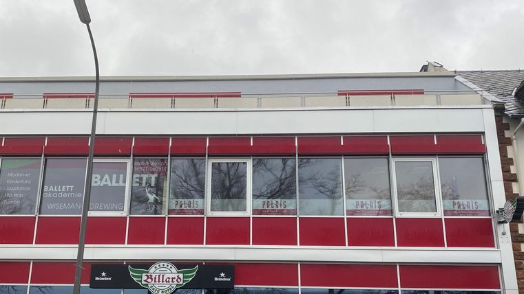 Een modern gebouw met rode en witte gevel elementen. De ramen zijn groot en goed zichtbaar, en er is een bord bij de ingang.