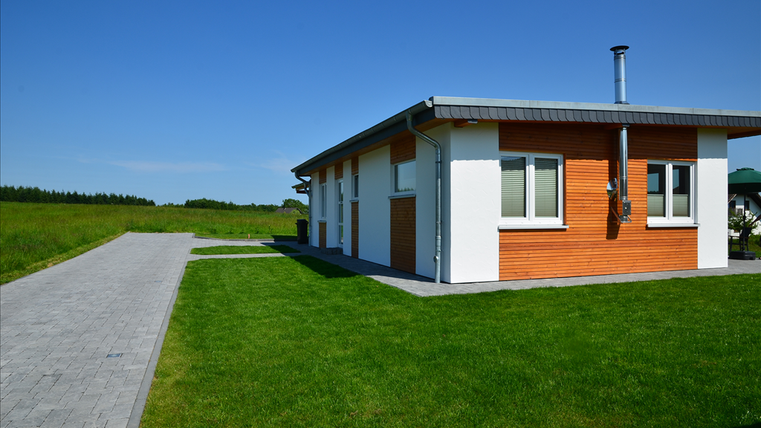 A modern single-family house with a combination of wooden and plaster facade. The garden is well-maintained and surrounded by a green lawn.