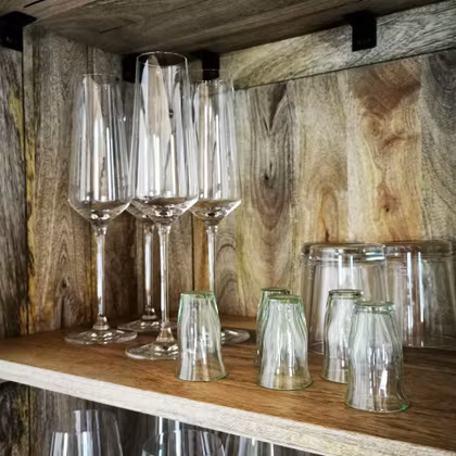 Een houten rek met verschillende glazen. Boven staan lange champagneglazen en onder kleine kleurrijke glazen.