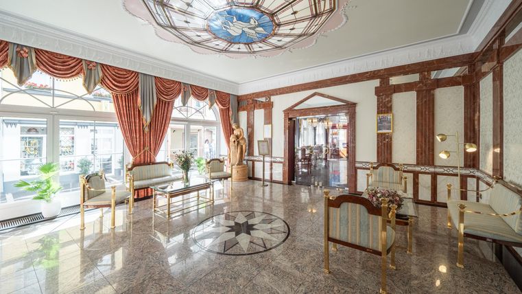 Een elegante lobby met een marmeren vloer en rijk versierde ramen. De smaakvolle inrichting en de kunstwerken geven het een luxueuze charme.