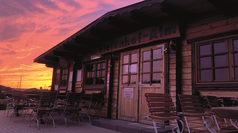 Terras van de Bielenhof Alm met houten banken voor het houten gebouw. Kleurrijke lucht door de ondergang van de zon op de achtergrond.