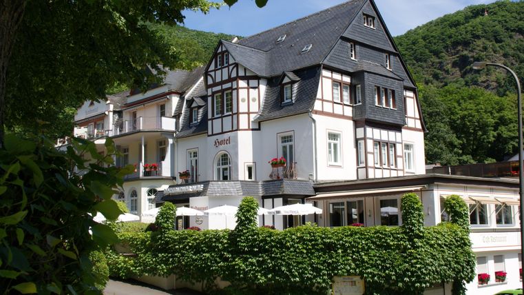 Een charmant vakwerkhuis omringd door groene planten. De omgeving toont zachte heuvels en een uitnodigende sfeer.