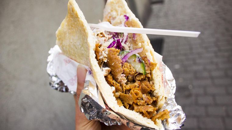 Ein Döner in einer Hand gehalten, gefüllt mit Fleisch, Salat und Soße, in Alufolie eingewickelt.