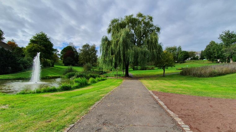 Ein schöner Park mit einem Parkplatz und einem Teich. Im Hintergrund steht ein Wasserfall und viele grüne Bäume.