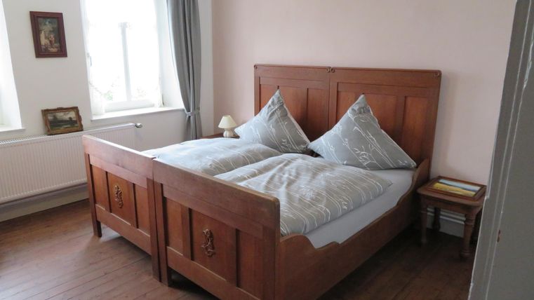 Ein gemütliches Schlafzimmer mit einem Holzbett und zwei Kissen. Die Wände sind in einem zarten Farbton gestrichen und es gibt ein Fenster mit Vorhängen.