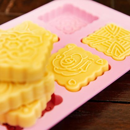 Eine Form mit gelb gefärbten Süßigkeiten, die verschiedene Muster zeigen. Die Form hat mehrere Fächer und ist rosa.