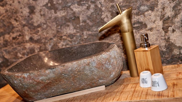 An elegant stone sink with a golden faucet. Next to it stands a wooden bottle and two small containers.
