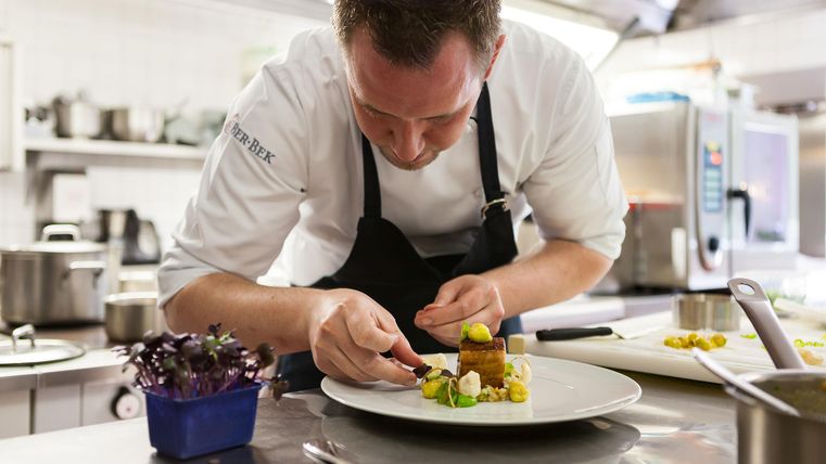 Ein Koch dekoriert einen Teller in einer modernen Küche. Die Präsentation des Gerichts ist sorgfältig und kunstvoll.