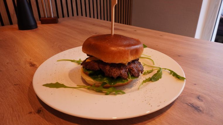 A juicy burger with a soft bun and fresh arugula. The dish is placed on a white plate and contrasts with the wooden surface.