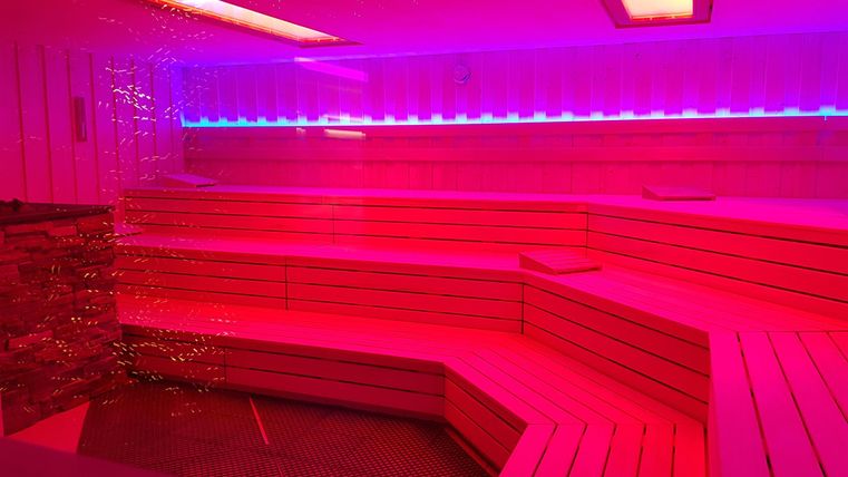 Ein modernes Wellnessbereich mit roten und blauen Lichtern. Die Holzsitze sind in einem stilvollen Design angeordnet.