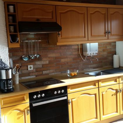 Eine gemütliche Küche mit holzfarbenen Küchenmöbeln und modernen Geräten. Die Wände sind mit ansprechenden Fliesen dekoriert.