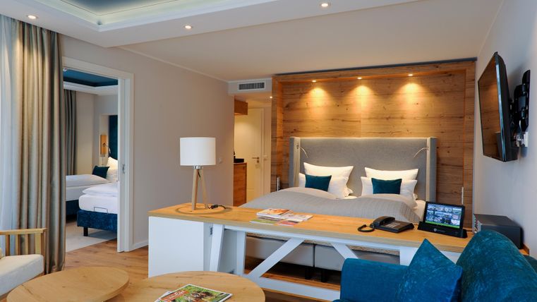 Ein modernes Zimmer mit einem komfortablen Doppelbett und eleganten Holzdetails. Der Raum ist hell und angenehm eingerichtet mit einem Sitzbereich und einem Tisch.