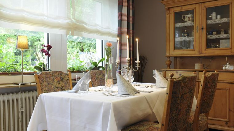 Ein einladender Essbereich mit einem schön gedeckten Tisch und bequemen Stühlen. Die Fenster lassen viel natürliches Licht herein und das Zimmer ist geschmackvoll eingerichtet.