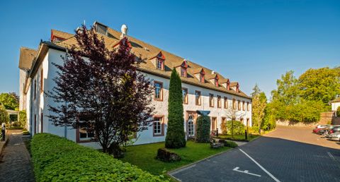 Ein modernes Gebäude mit weißen Wänden und roten Fenstern. Der Garten ist grün mit Bäumen und Sträuchern.